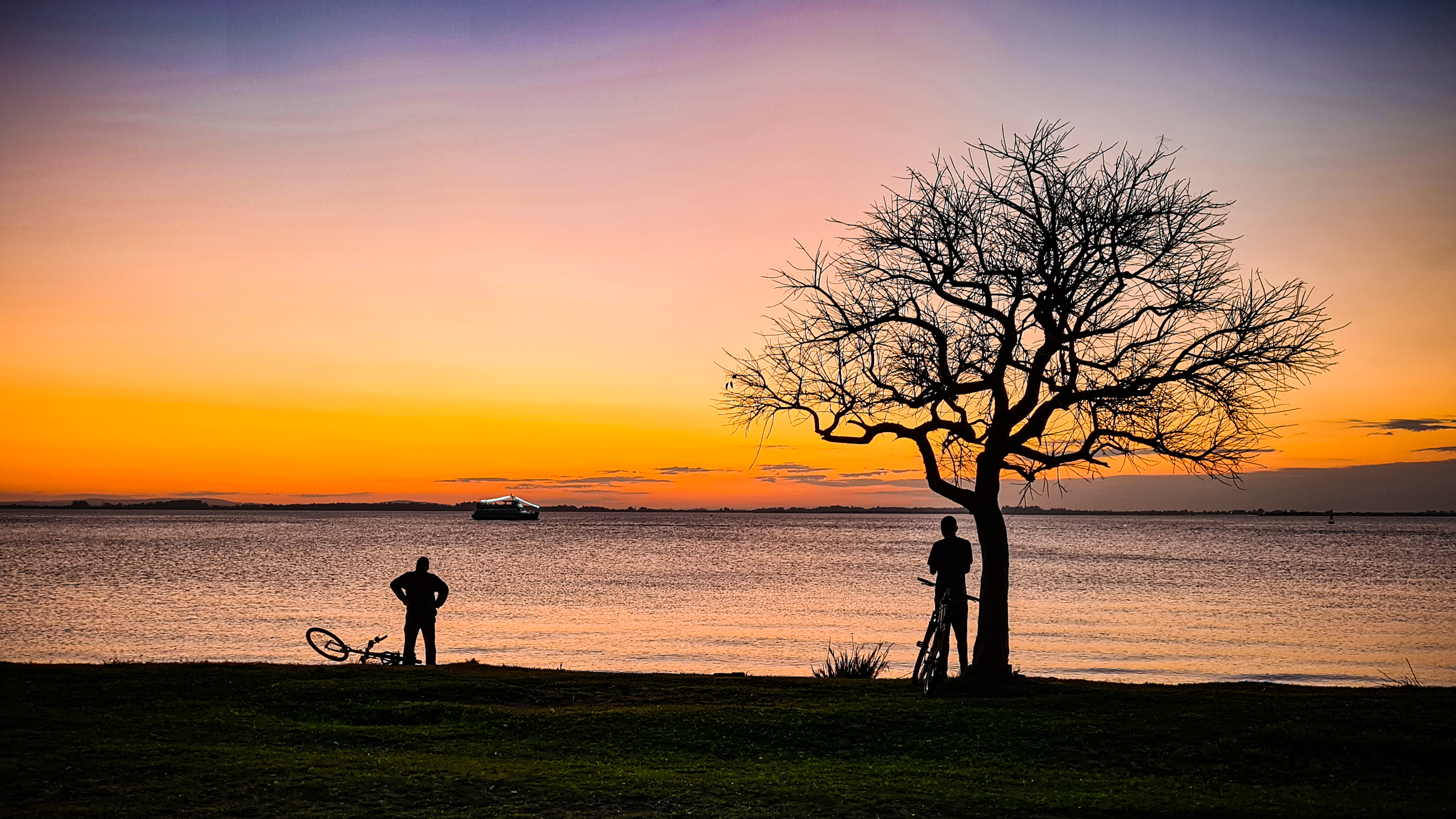 sunset with silhouette of two man and a tree at river bank